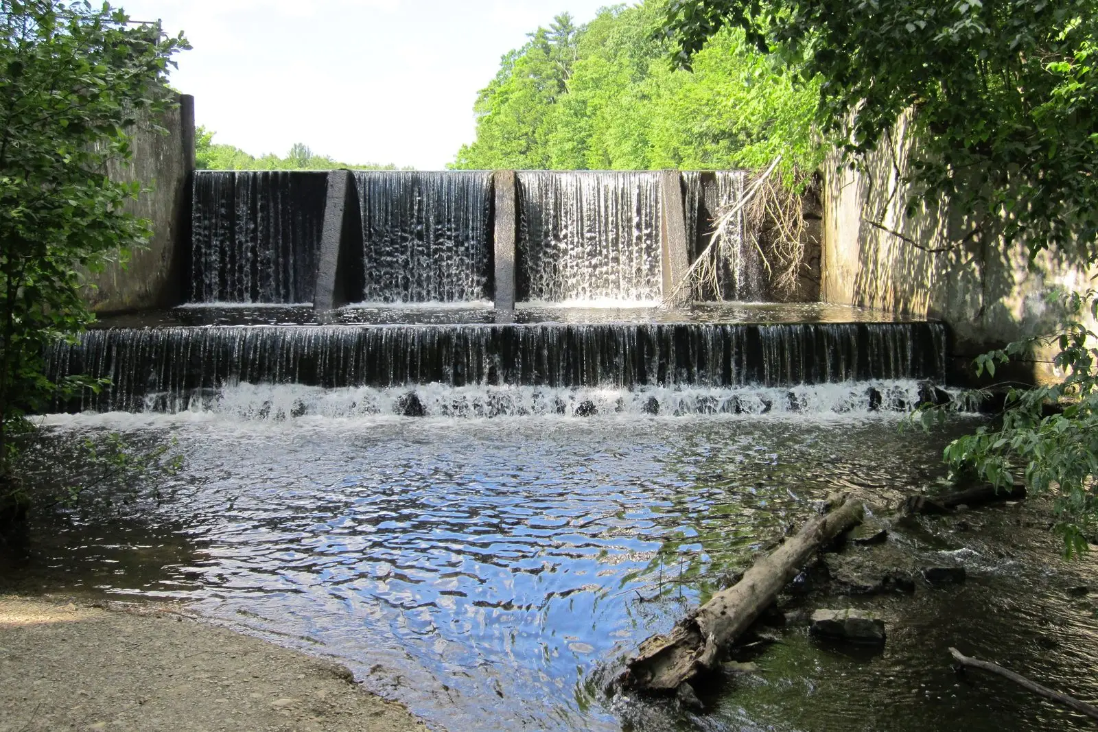 Water pouring over a concrete spillway into a creek pool at the East Greenbush town park