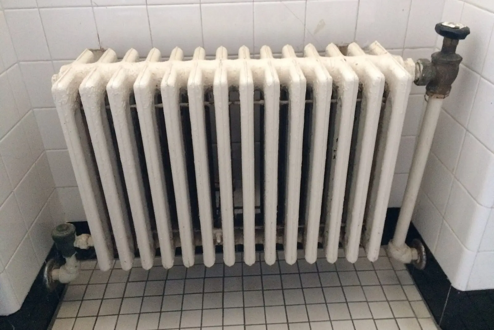 White painted cast iron radiator with a brass valve in an older tiled room